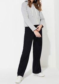 Sudadera gris recortada con cremallera frontal y cordones blancos, combinada con pantalones anchos de rayas negras y deportivas blancas.