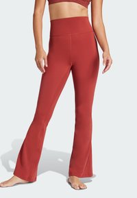 Leggings flare taille haute rouges en matière extensible, avec des coutures plates et une texture lisse, conçus pour le confort et la liberté de mouvement.