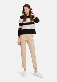 Gestreifter Pullover in Schwarz und Beige, Strickstoff, weitem Ausschnitt, kombiniert mit beigefarbenen Tailorpants und weißen Sneakers. Lässiges Outfit.