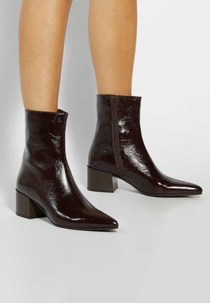 Brown patent leather ankle boots with a pointed toe, block heel, and side zipper detail. Smooth texture with a shiny finish.