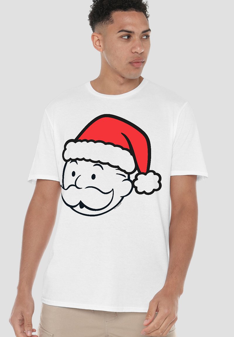 Young man wearing a white T-shirt with a cartoon Santa Claus face in a red hat, looking to his left against a plain background.