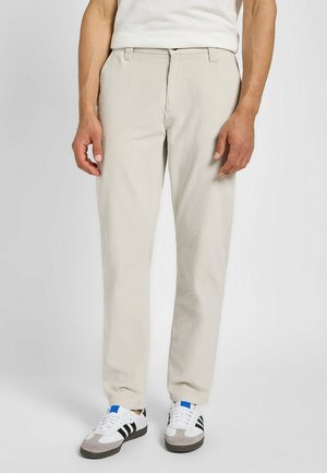 Jasno beżowe spodnie z kordurowego materiału o prostym kroju, z subtelnymi pionowymi prążkami. W zestawieniu z białymi sneakersami z czarnymi paskami.