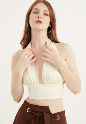 Crème halter neck top met diepe halslijn en geraffineerde bodice, gecombineerd met bruine high-waisted broek met een strik in de taille en oogje-detail.