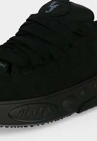 Close-up of a black sneaker with thick laces and embossed sole text reading "01 of one" and decorative symbols.