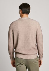 Vaaleanbeige ribattu neulepaita pitkillä hihoilla ja pyöreällä kaula-aukolla, jossa on teksturoitu pinta ja istuva vyötärö.