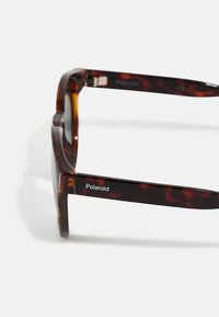 Tortoiseshell sunglasses with a thick frame, featuring a polished texture. "Polaroid" logo located on the black accent of the arm.