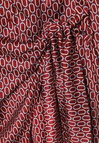 Material roșu cu model de zale în alb și albastru deschis. Prezintă o textură netedă, lucioasă, cu un detaliu de nod pe o parte.