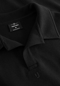 Fekete póló, textúrált anyagból, hajtott gallérral. A címkén "JOHNNY URBAN" felirat, "M" méret és "MADE IN TÜRKİYE" található.