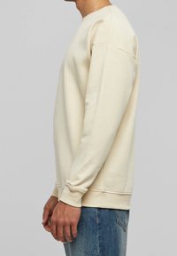 Felpa beige chiaro con maniche lunghe e polsini a coste, caratterizzata da uno scollo tondo classico e un tessuto morbido e strutturato.