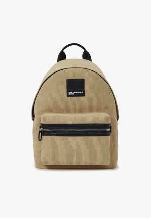 Rucsac bej din catifea cu o formă rotunjită, buzunar cu fermoar negru și patch cu logo. Dispune de o mânere superioară și bretele ajustabile.