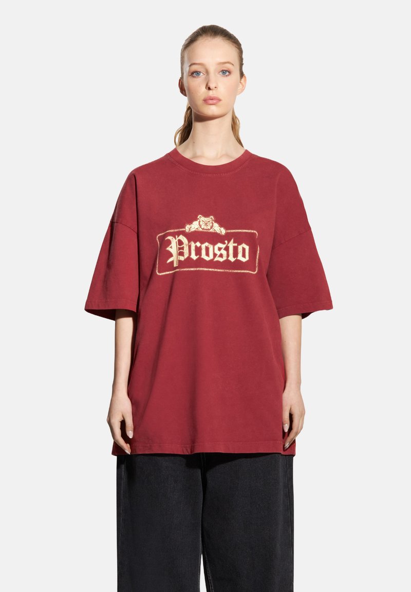 Bordowa, oversize koszulka z bawełny, z wyróżniającym się kremowym logo "Prosto" na przodzie. Krótkie rękawy i okrągły dekolt.