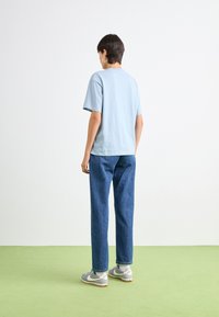 T-shirt en coton bleu clair à manches courtes, associé à un jean en denim bleu ample et des baskets grises. Design sobre, sans motifs.