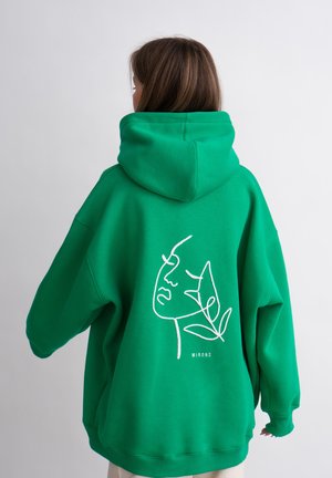 Groene hoodie met grote capuchon, voorzien van een witte lijntekening van een gezicht en een blad op de achterkant. De stof lijkt zacht en heeft een ontspannen pasvorm.