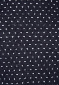 Marinblått tyg med en texturerad yta, prydd med små vita prickar som är jämnt fördelade. Lämpligt för kläder eller tillbehör.