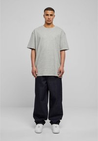 Grå oversized t-skjorte laget av bomull, kombinert med løse mørke denimbukser. Hvite sneakers fullfører antrekket. Enkelt design, ingen mønstre.