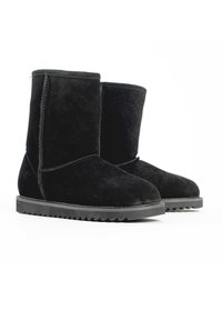 Botas de tobillo de ante negro con puntera redondeada, suela de goma plana y un diseño simple y sin adornos. Costura a lo largo de los lados.
