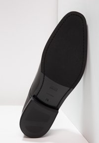 Semelle de chaussure en cuir noir avec semelle en caoutchouc texturée et accents de couture ; présente le logo de la marque et la taille "7½" embossés sur la semelle intérieure.