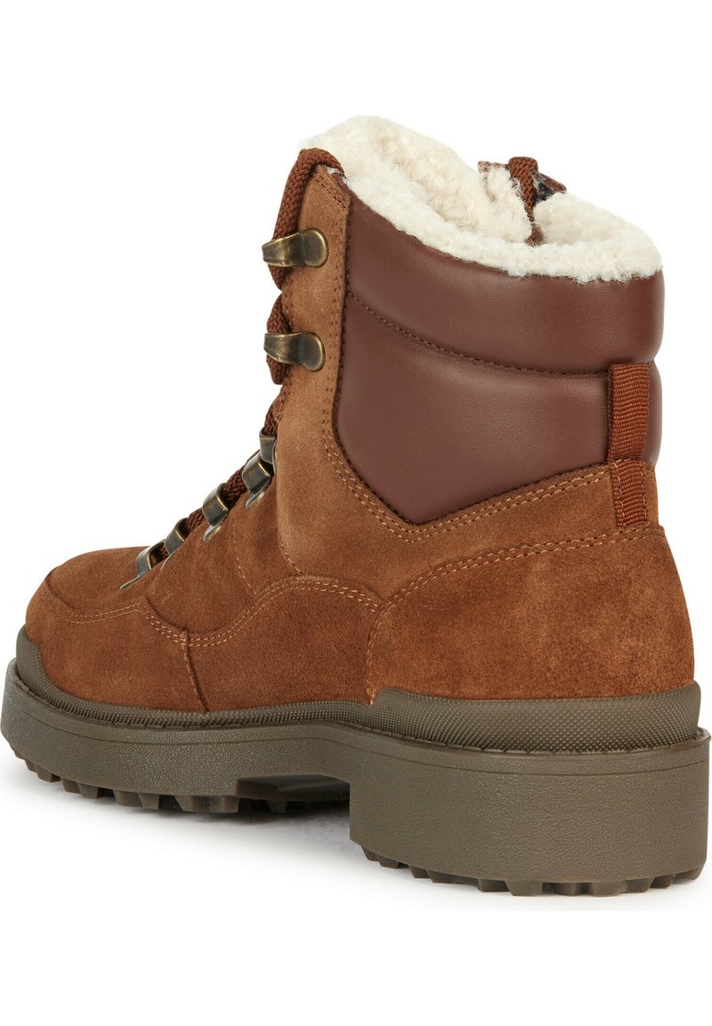 Botte chelsea en cuir suédé marron avec un col rembourré en cuir marron, des œillets en métal et une semelle en caoutchouc texturée. Doublée en fausse fourrure douce.