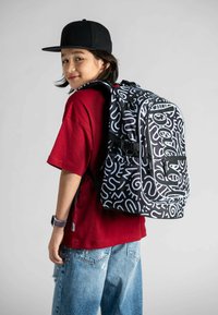 Zaino in bianco e nero con motivi astratti; presenta spallacci regolabili, una tasca con zip e un design in tessuto resistente.