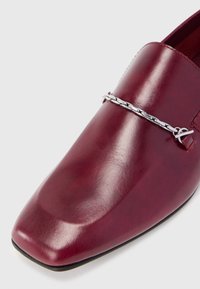 Burgunderfarvet lædersandal med firkantet tå og sølvkædedetalje på oversiden, på en hvid baggrund.