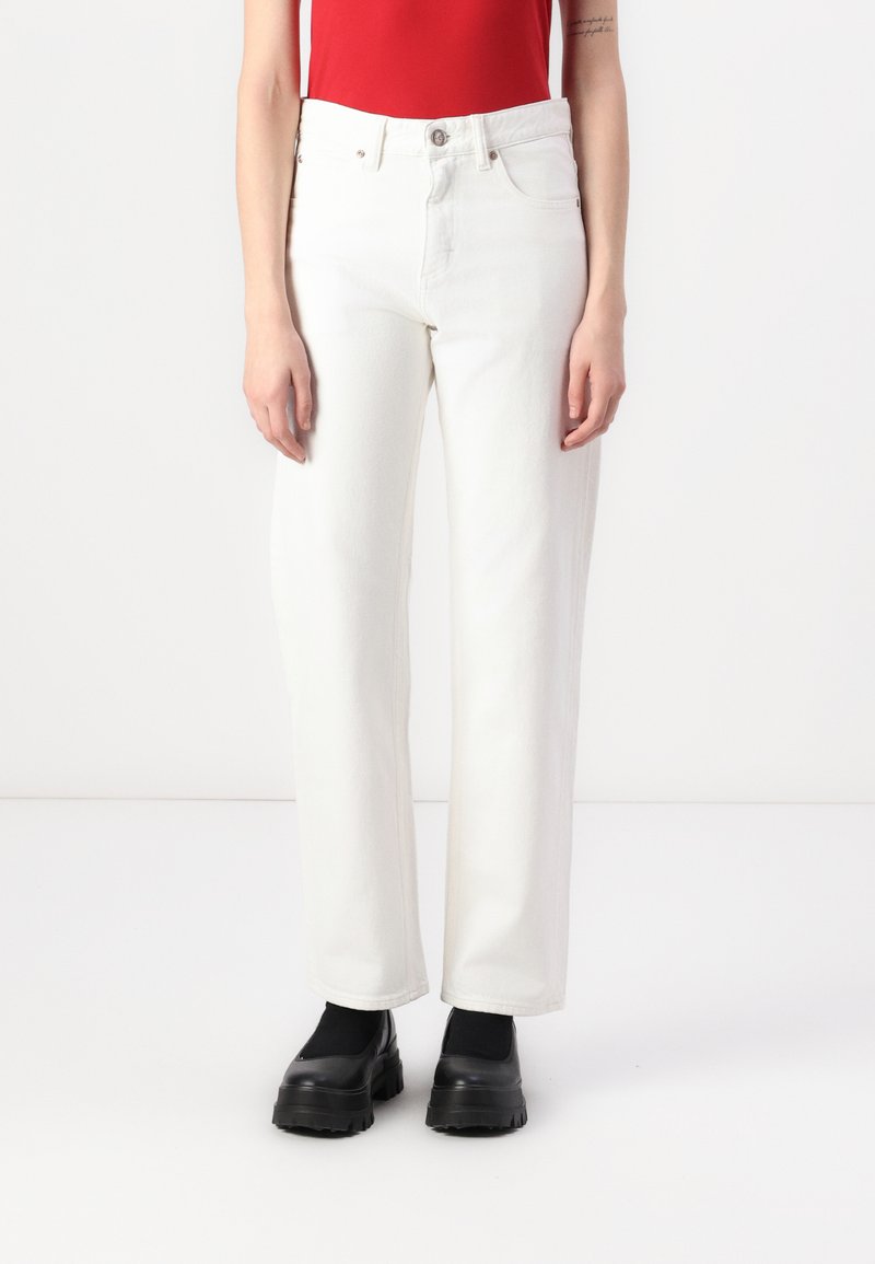 Vit denim rak benbyxor med hög midja, fem fickor och stängning framtill med knapp, i kombination med svarta platåskor.