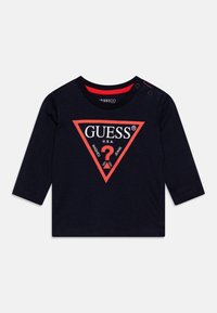 Navy long-sleeve T-shirt with red triangular logo featuring "GUESS® U.S.A." text, shoulder snaps, and a soft cotton texture.