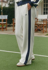 Baltos laisvalaikio kelnės su tamsiai mėlynu dryžiu šone, su priekinė kišene ir siuvinėtu „self.“ logotipu. Minkšta medžiaga, laisvas kirpimas.