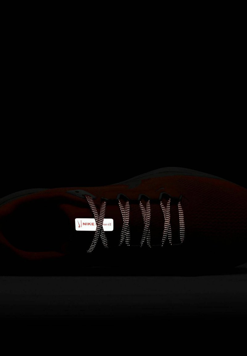 Baskets rouges avec un dessus texturé, des lacets réfléchissants et un logo Nike blanc sur la languette ; le fond sombre améliore la visibilité.