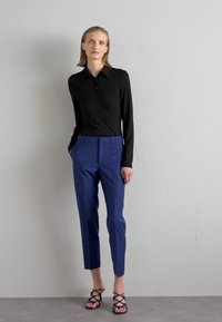 Cămașă neagră cu dungi, cu mânecă lungă și trei nasturi, asociată cu pantaloni negri închiși, ajustați. Sandale negre cu toc înalt completează ținuta.
