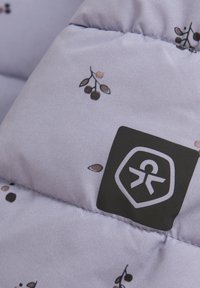 Ljubičasta jakna s perjem s uzorkom lišća. Ima crnu oznaku s logotipom sa stiliziranom figurom. Materijal izgleda glatko i blago sjajno.
