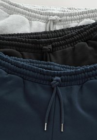 Tres pares de pantalones de chándal: gris, negro y azul marino, cada uno con una cintura elástica y cordón, que muestran una textura suave y una construcción resistente.