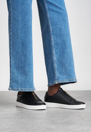Svarta lädersneakers med vit sula, med en detaljerad dragkedja fram. Parat med blå vida denimjeans.