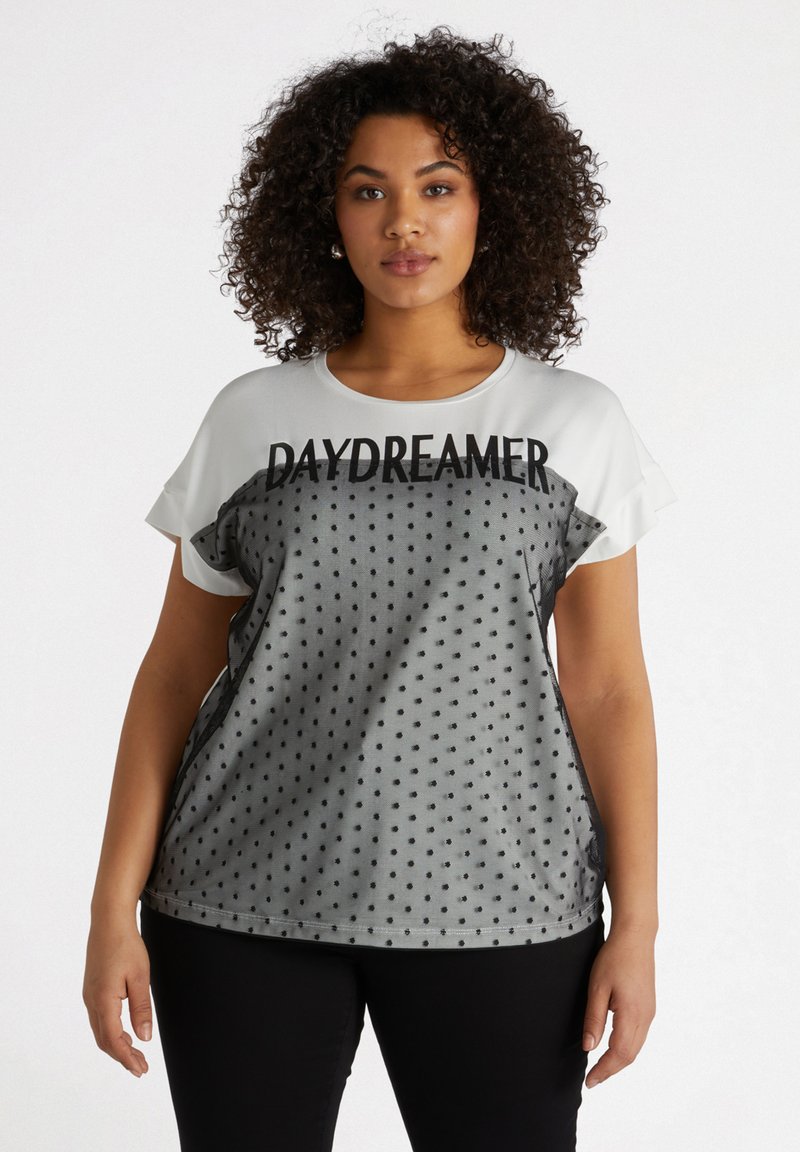 Camiseta gris de manga corta con un patrón de lunares negros, cuello redondo y el texto "DAYDREAMER" en negrita negra en la parte delantera.