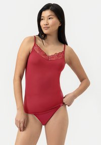 Camisole rouge avec des bretelles réglables, présentant une bordure en dentelle avec des motifs floraux au niveau du col et un tissu lisse et extensible sur l'ensemble.