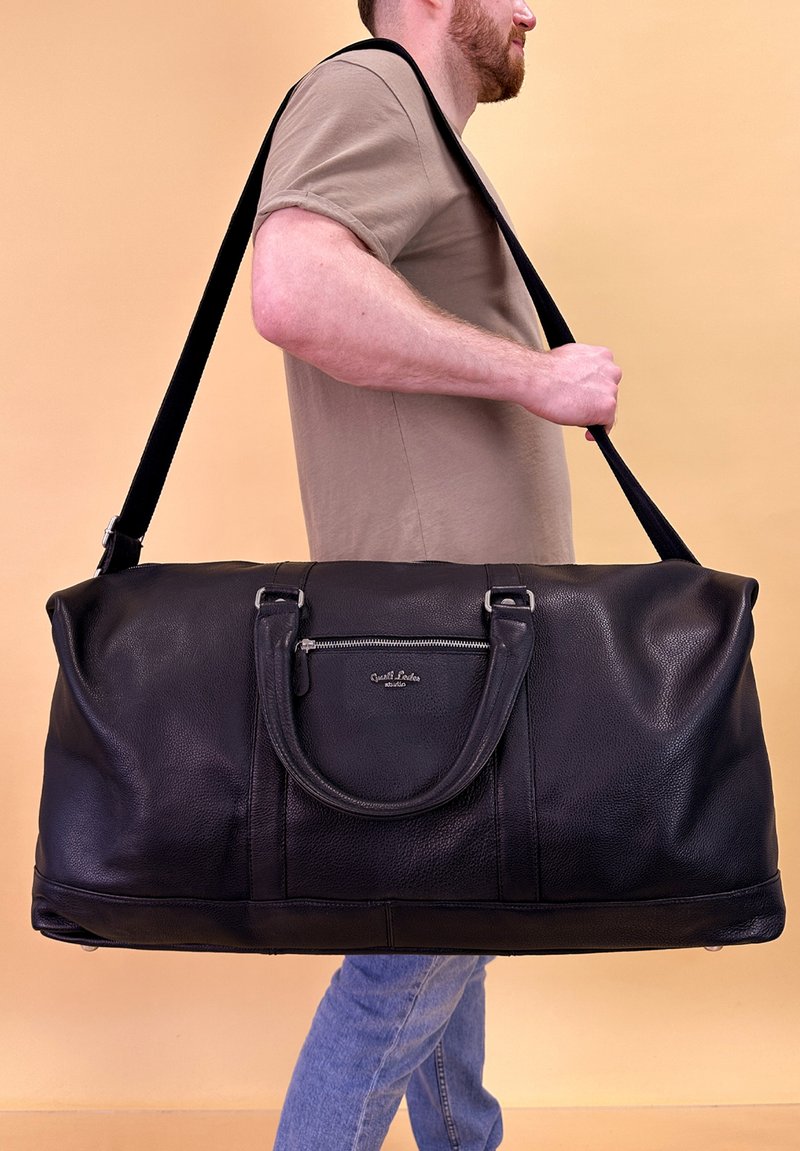 Sort læder duffelbag med tekstureret overflade, dobbelte top hændtag, justerbar skulderrem og en frontlomme med lynlås.