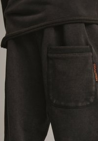 Czarne dresy bawełniane z kieszenią boczną z rypsową lamówką oraz pomarańczowym logo „COALITION” na dole nogawki. Miękki, teksturowany materiał.