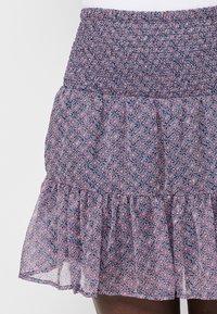 Gonna a fantasia floreale realizzata in tessuto leggero; presenta una vita arricciata, orlo con ruches e colori alternati di rosa e blu navy.