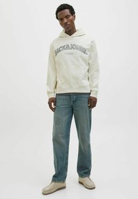 Felpa crema con logo "JACK & JONES", materiale morbido, tasca a marsupio, abbinata a jeans azzurri chiari e scarpe slip-on beige.