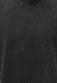 Μαύρο T-shirt με στρογγυλή λαιμόκοψη, ξεθωριασμένη, ελαφρώς φθαρμένη υφή και ορατά ραφές γύρω από τον γιακά.