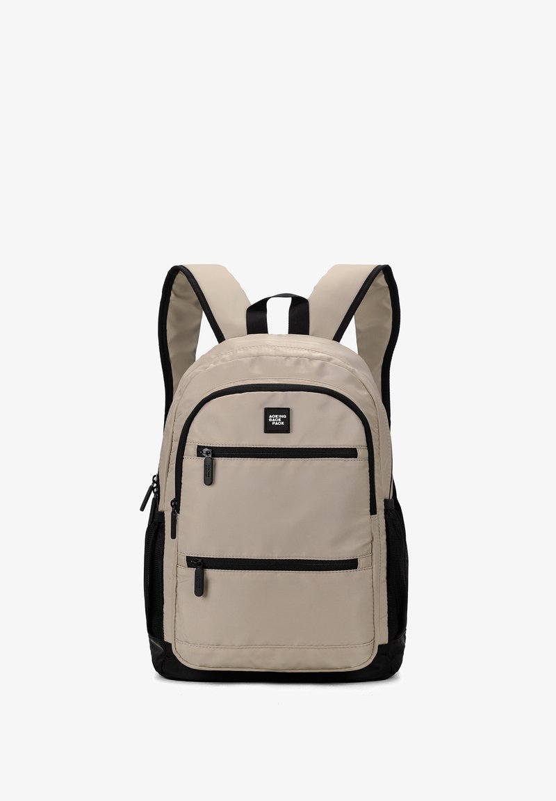 Sac à dos beige avec des accents noirs, doté de bretelles rembourrées, de plusieurs poches zippées et d'un petit logo à l'avant.