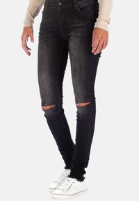 Jeans skinny neri con dettagli strappati alle ginocchia, realizzati in denim. Abbinati a una maglietta a maniche lunghe di colore chiaro e sneaker bianche.