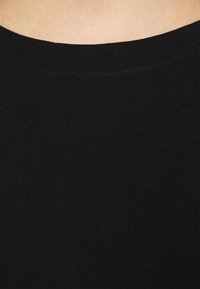 Musta puuvillapaita pyöreällä pääntiellä. Kangas on sileä ja joustava, ja se esittelee tiiviin istuvuuden ilman kuvioita tai yksityiskohtia.