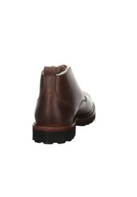 Bottine en cuir marron avec une finition lisse, bout rond, coutures renforcées, semelle extérieure rouge contrastante et doublure douce visible sur le dessus.