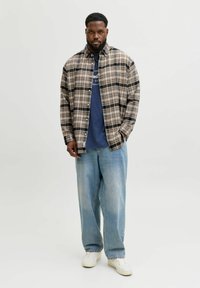 Kariertes Flanellhemd in Beige und Marineblau, über einem marineblauen Grafik-T-Shirt getragen, kombiniert mit hellblauen lockeren Jeans und weißen Sneakers.
