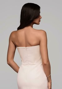 Šaty bez ramínek, přiléhavého střihu z jemné béžové látky se hladkým povrchem, s diskrétním zipovým detailem na zadní straně a vytvarovanou siluetou.