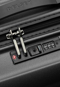 Close-up van de zwarte DELSEY koffer ritssluiting met TSA-goedgekeurd cijferslot ingesteld op 0-0-9 en dubbele metalen ritshandvatten.