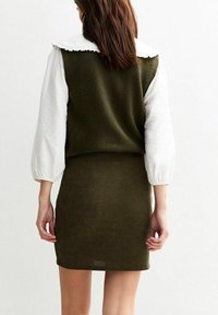 Vestido de punto verde oliva con una textura acanalada, que presenta un top blanco con cuello rizado y mangas abullonadas para un look en capas.