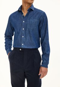 Donkerblauwe denim overhemd met lange mouwen, knoop-kraag, voorzak, gecombineerd met donker marineblauwe broek met knoopsluiting.