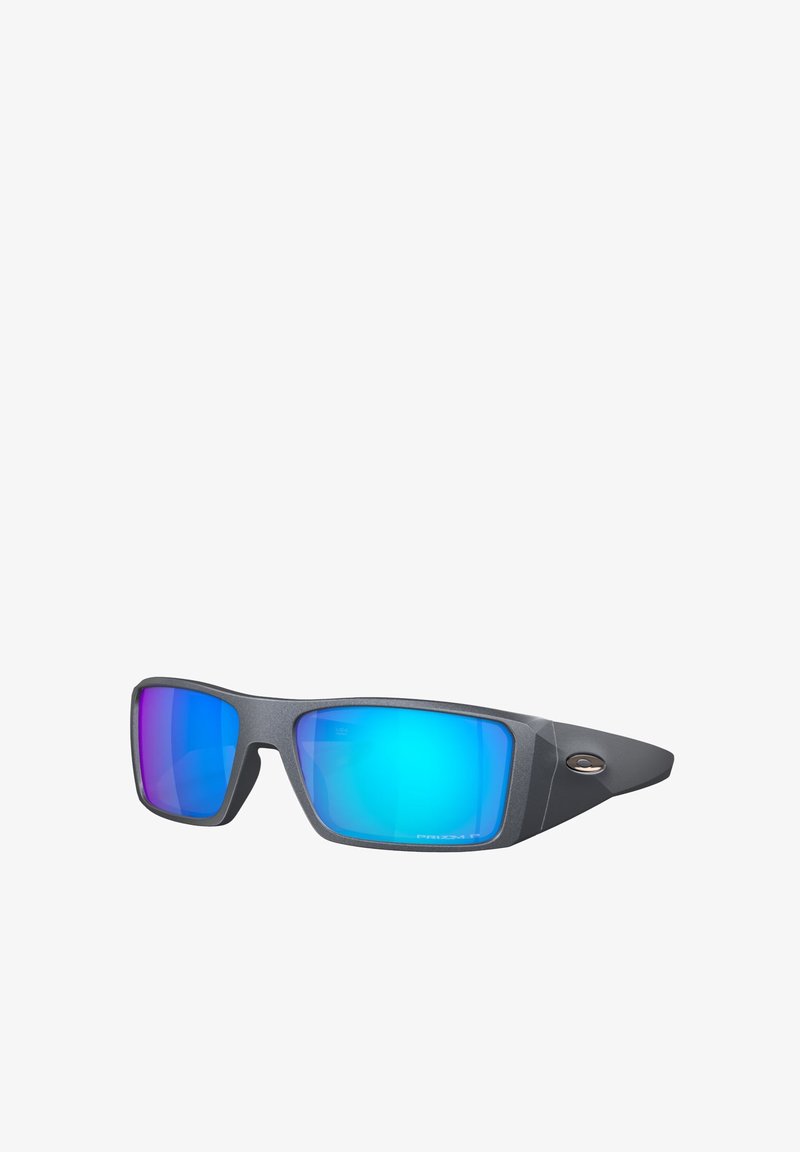 Occhiali da sole con montatura nero opaco, lenti rettangolari con una sfumatura blu e viola, e un piccolo logo sul lato.