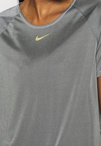Šedé sportovní tričko s horizontální jemnou strukturou, kulatým výstřihem, krátkými rukávy a malým žlutým logem Nike na hrudi.